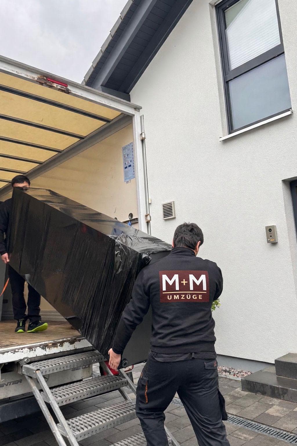 M+M Umzüge Team lädt verpackten Fernseher über Rampe in den LKW