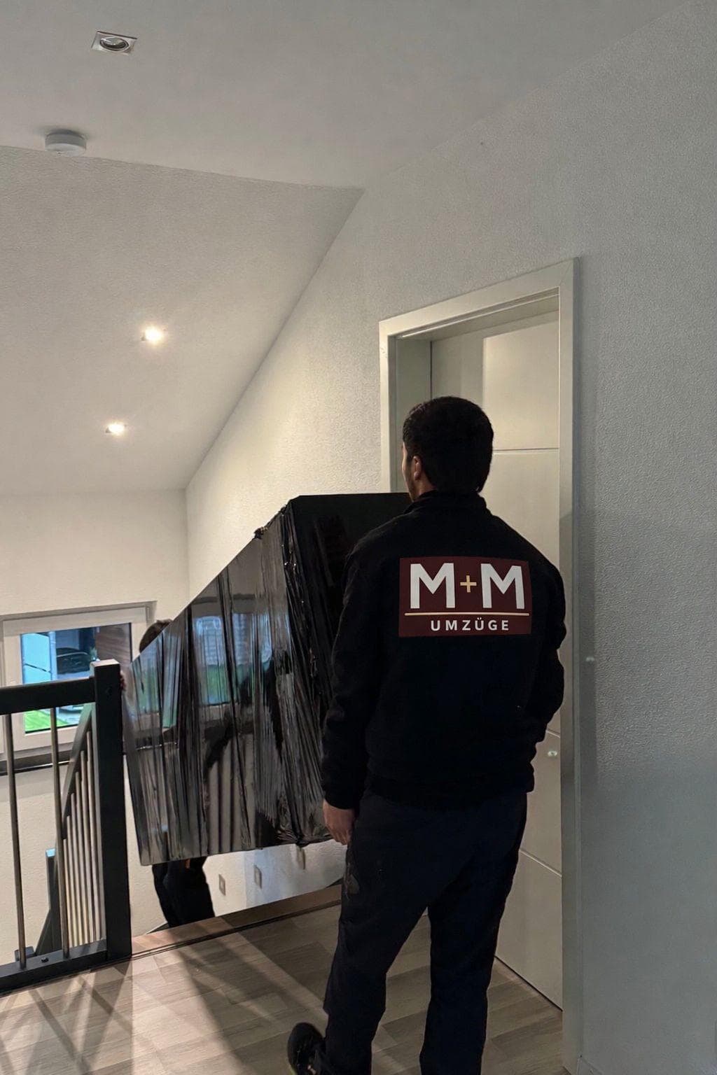 M+M Umzüge Mitarbeiter trägt verpackten Fernseher sicher ins Obergeschoss